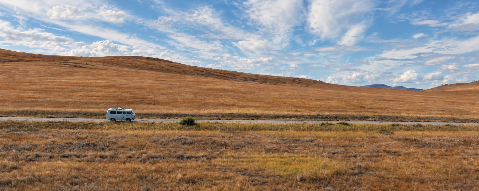 A Bukhanka van on a road among Tuva’s steppe hills under a cloudy sky