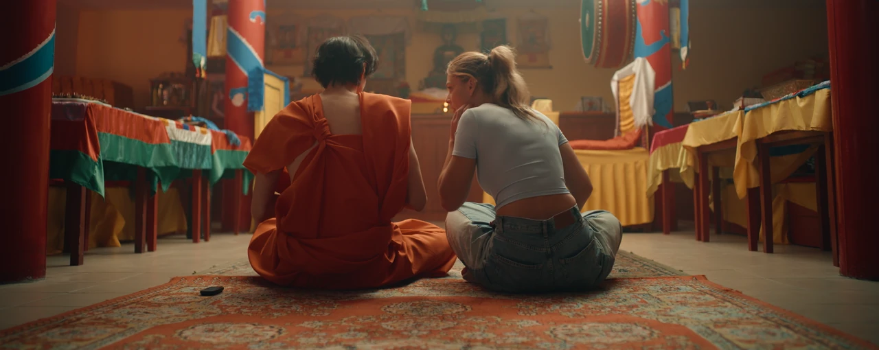 A woman and a Buddhist monk sit with their backs to the viewer inside a temple.