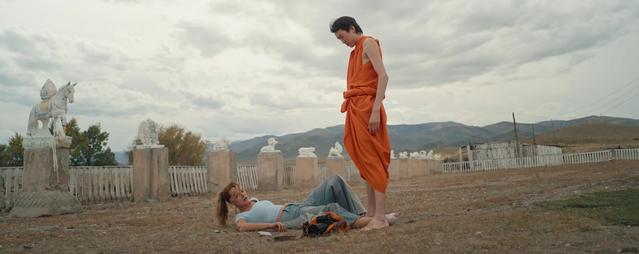 A woman lies on the ground beside a monk in the courtyard of a Buddhist temple.