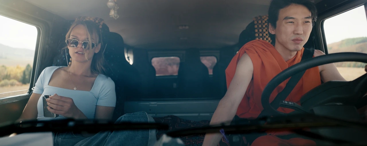 A woman wearing sunglasses sits beside a monk driving a UAZ van.